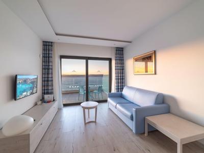 Helles Wohnzimmer mit Sofa, kleinem Tisch, Fernseher und großem Fenster mit Blick auf die Landschaft.