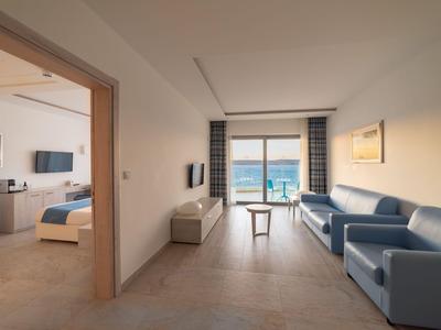 Helles Hotelzimmer mit Wohnzimmer, blauen Sofas und Meerblick durch große Fenster.