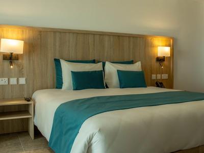 Gemütliches Hotelzimmer mit großem Bett, Holzkopfteil und stilvollen Wandlampen.