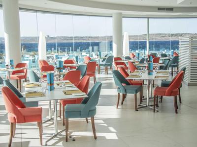 Helles Restaurant mit bunten Stühlen und großem Fenster mit Meerblick.