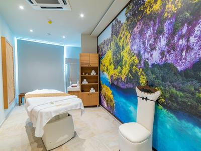 Modern eingerichteter Massageraum mit Liege und großem Wandbild einer tropischen Küstenlandschaft.