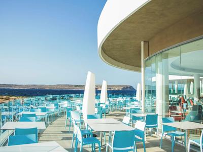 Offene Terrasse mit blau-weißen Stühlen und Tischen neben einem modernen Gebäude mit Panoramablick.