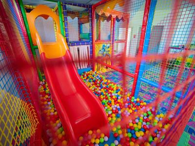 Kolorowy plac zabaw w pomieszczeniu z czerwoną zjeżdżalnią i basenem z piłeczkami w hotelu.