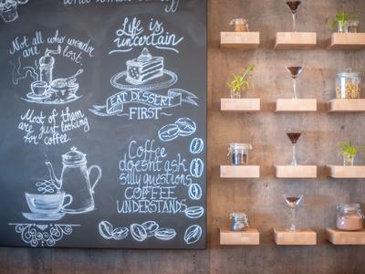 Kaffeethema an Schiefertafel neben minimalistischen Holzwandregalen mit kleinen Pflanzen und Deko.