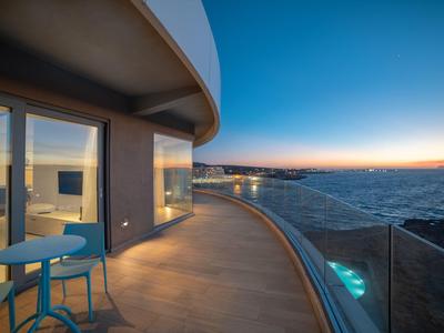 Nowoczesny taras hotelowy z miejscami do siedzenia i widokiem na morze o zachodzie słońca.