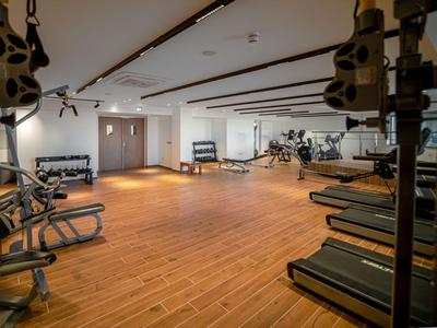 Heller Fitnessraum mit Holzfußboden und verschiedenen Trainingsgeräten an den Wänden.