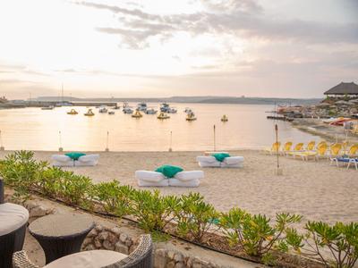 Strand mit Liegestühlen, Sonnenschirmen und Booten auf ruhigem Wasser bei Sonnenuntergang.