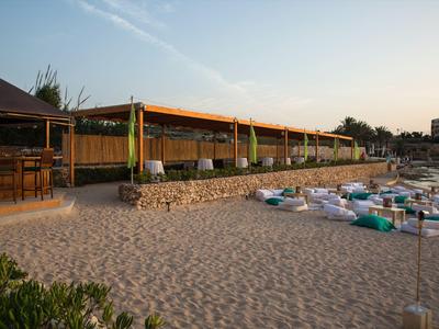 Strandbar mit Sitzgelegenheiten und Lounge-Kissen am Sandstrand bei Sonnenuntergang.
