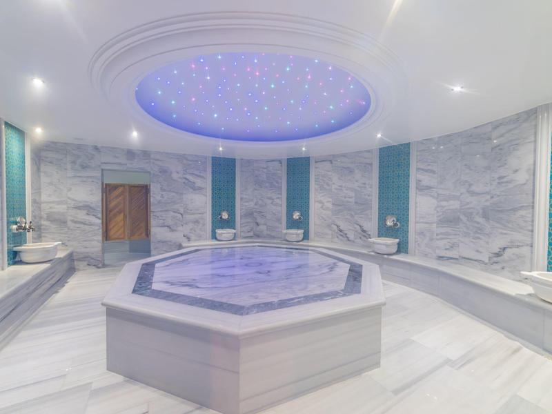 Wnętrze luksusowych łaźni tureckich z centralnym basenem i sufitem z gwiazdami.