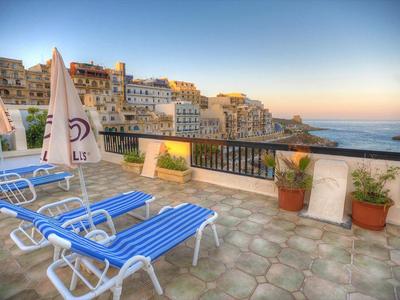 Blick auf eine Terrasse mit blauen Liegestühlen und Stadtgebäude im Hintergrund bei Sonnenaufgang.