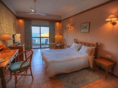 Camera d'hotel accogliente con letto matrimoniale, scrivania, sedie e balcone con vista mare.