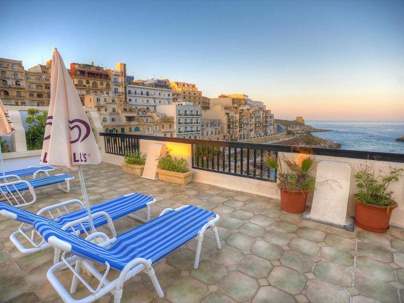 Vista di una terrazza con lettini blu e edifici della città sullo sfondo all'alba.