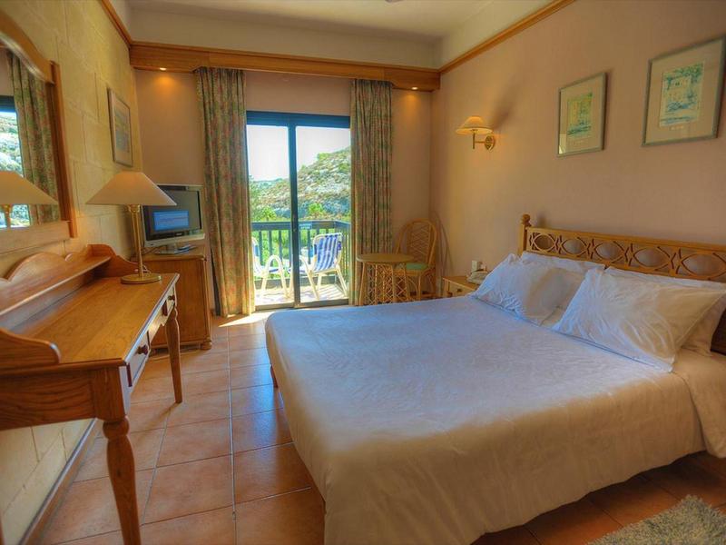 Camera d'hotel accogliente con letto matrimoniale, scrivania, TV e balcone con vista sul verde.