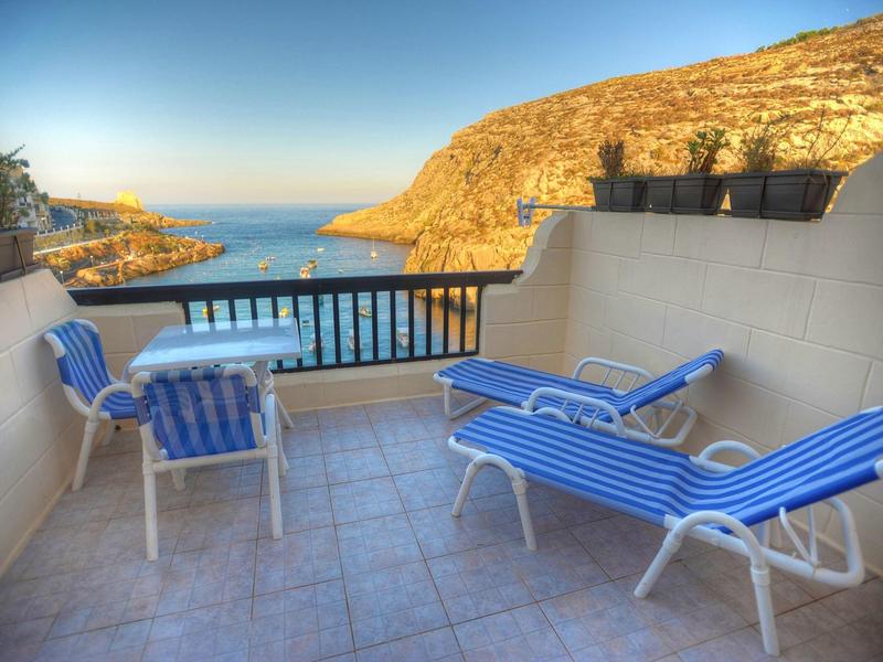 Balcone con lettini e sedie a righe blu e bianche con vista sul mare e sulle colline soleggiate.