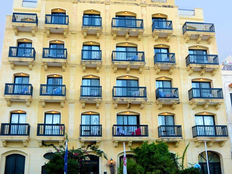 Edificio alberghiero pluripiano con balconi e facciata gialla sotto un cielo limpido.