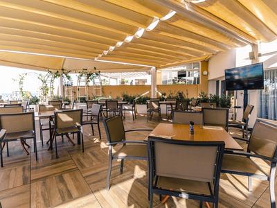 Überdachte Hotelterrasse mit Tischen, Stühlen und TV-Bildschirm bei Tageslicht