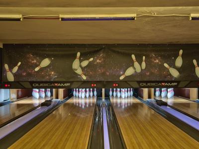 Blick auf eine Bowlingbahn mit leuchtenden Pins und hölzernem Boden in einer Halle.