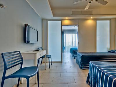 Hotelzimmer mit zwei Betten, blauen Stühlen und Flachbildfernseher, Blick zum Balkon