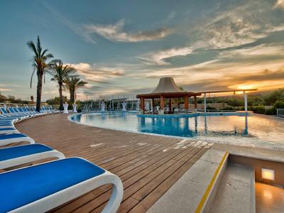 Poolbereich mit Liegestühlen und Palmen bei Sonnenuntergang in einem Hotelresort