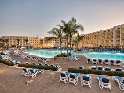 Großer Hotelpool mit Liegestühlen und Palmen bei Sonnenuntergang