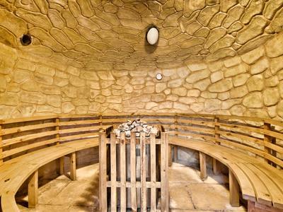 Runder Saunaraum mit Steinen an der Wand und Holzbank zum Sitzen.