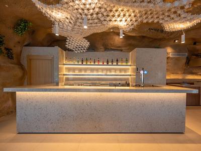 Moderner Hotelbarbereich mit beleuchtetem Tresen und organisch gestaltetem Holzdekor an der Decke.