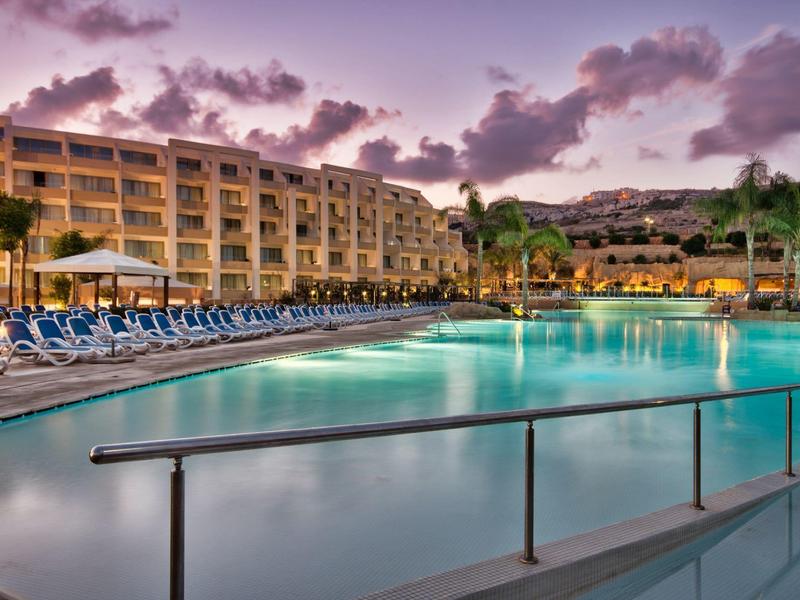 Großer Hotelpool bei Sonnenuntergang mit Liegestühlen und umliegenden Gebäuden.