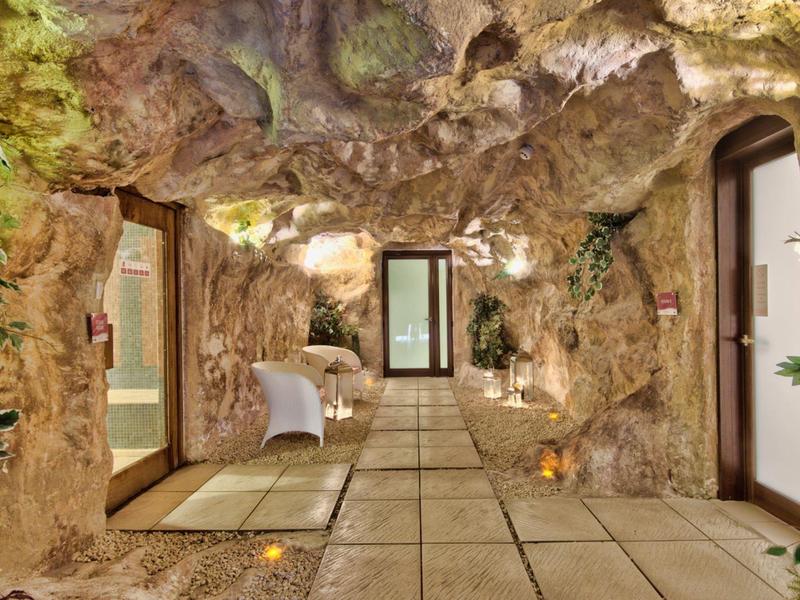 Flur mit felsartigen Wänden und Türen, dekoriert mit Pflanzen und Kerzenlicht.