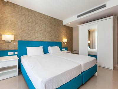 Modernes Hotelzimmer mit zwei Betten, blauen Kopfenden, Nachttischen und kleinem Schrank mit Spiegel.