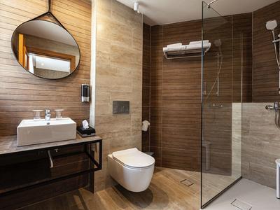 Modernes Badezimmer mit runder Spiegel, Waschbecken, Toilette und begehbarer Dusche mit Glasabtrennung.