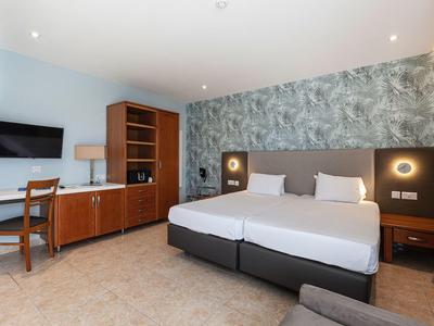 Modernes Hotelzimmer mit Doppelbett, Schreibtisch, Fernseher und dekorativer Wandgestaltung.