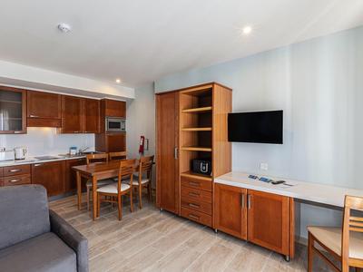 Wohnbereich eines Hotelzimmers mit Küchenzeile, Essplatz und Fernseher an der Wand.