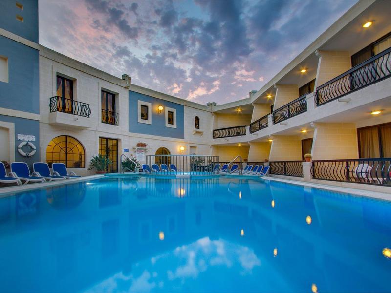 Innenhof eines Hotels mit blauem Swimmingpool, Sonnenliegen und mehrstöckigen Gebäuden bei Dämmerung.