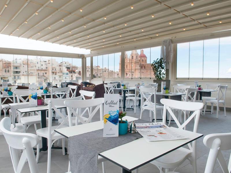 Hell und luftiges Restaurant mit weißen Möbeln und Meerblick unter einem überdachten Terrassendach.