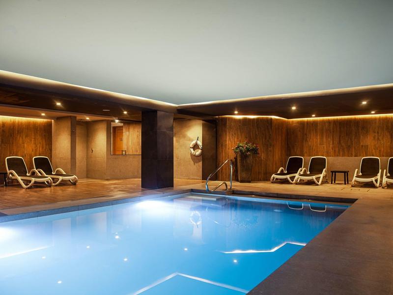 Innenpool mit Holzverkleidung und Liegestühlen in einem entspannten Wellnessbereich.