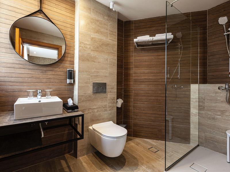 Modernes Badezimmer mit runder Spiegel, Waschbecken, Toilette und begehbarer Dusche mit Glasabtrennung.