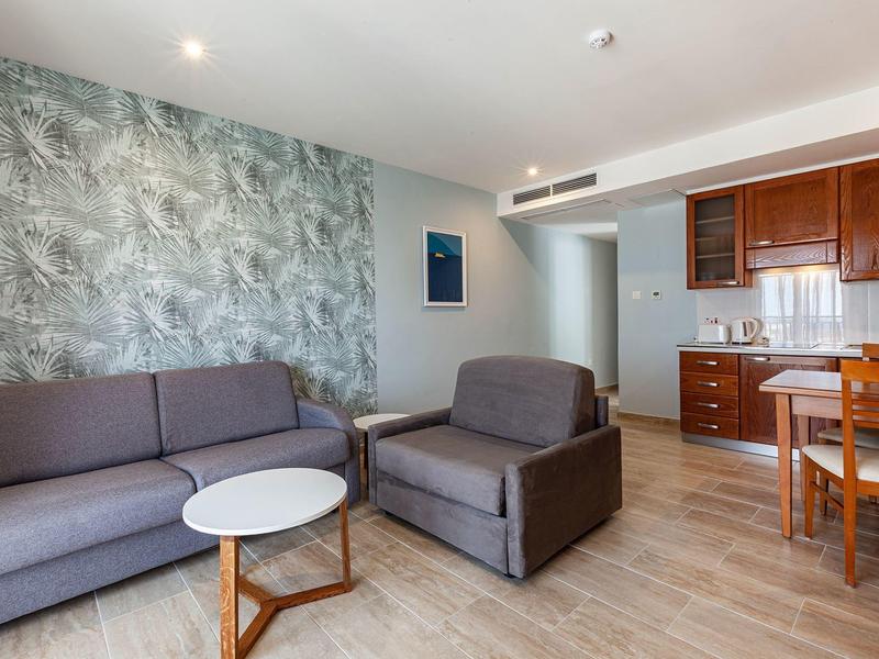 Moderne Hotelzimmer mit Sitzbereich, grauem Sofa, Sessel, Küchenecke und Esstisch.