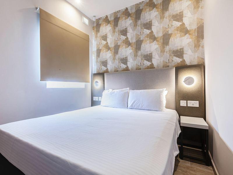 Modernes Schlafzimmer mit Doppelbett, grauem gepolstertem Kopfteil und gemusteter Tapete.