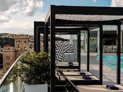 Area piscina moderna con lettini e ringhiera in vetro con vista su una città e una torre.
