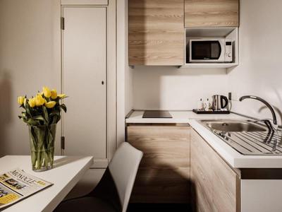 Kleine moderne Küche mit Holzmöbeln, Mikrowelle, Spüle und Blumen auf dem Tisch.