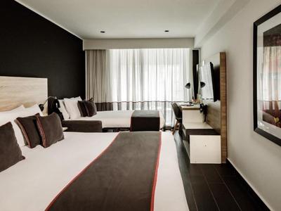 Modernes Hotelzimmer mit Doppelbett, Sitzecke und großem Fenster mit Vorhängen.