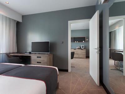 Modernes Hotelzimmer mit zwei Betten, Schreibtisch, Fernseher und Blick in angrenzenden Raum.