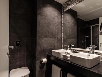 Modernes Badezimmer mit dunklen Wandfliesen, zwei Waschbecken und großem Spiegel.