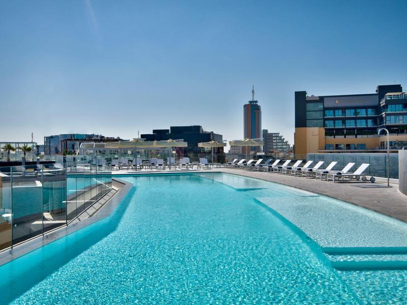 Moderner Hotelpool mit Liegestühlen und Stadtblick bei klarem Himmel