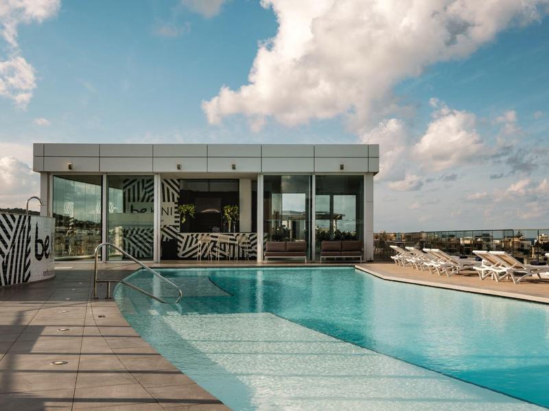 Moderner Poolbereich mit Glasgebäude und Liegestühlen unter bewölktem Himmel