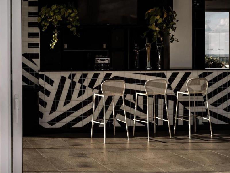 Drei hohe Stühle stehen vor einer schwarz-weißen Theke mit geometrischem Muster in einem modernen Innenraum.