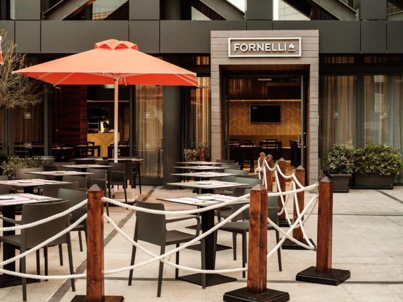 Leere Terrasse eines Cafés mit roten Sonnenschirmen und schwarzen Stühlen vor modernem Gebäude.