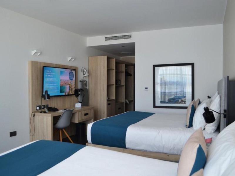 Hotelzimmer mit zwei Betten, Schreibtisch, Fernseher und modernem Interieur in kühlen Farben.