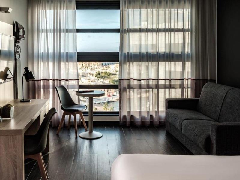 Modernes Hotelzimmer mit großen Fenstern, einem Tisch mit Stühlen und einem Sofa.