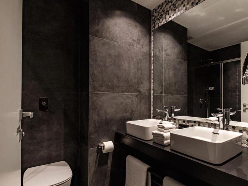 Modernes Badezimmer mit dunklen Wandfliesen, zwei Waschbecken und großem Spiegel.